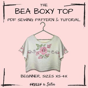 Puede incluir: Una camiseta blanca y holgada con un diseño floral en rosa y verde, colgada de una percha plateada. El texto de la imagen dice "THE BEA BOXY TOP PDF SEWING PATTERN & TUTORIAL BEGINNER, SIZES XS-4X SKULLS & Satin."