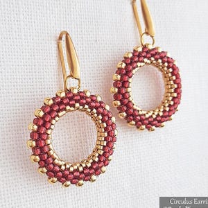 May include: Handmade hoop earrings with a red and gold beaded design. The earrings have a circular shape, with red beads on the outer edge and gold beads on the inner edge. Gold-coloured ear wires complete the design. The earrings are shown against a white backdrop.