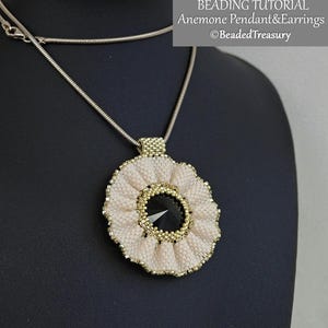 Peut inclure: Un collier pendentif Anémone perlé présenté sur un mannequin noir. Le pendentif est de couleur crème avec des accents dorés et une pierre centrale noire. Le collier a une chaîne argentée. Le texte sur l'image indique "BEADING TUTORIAL Anemone Pendant & Earrings ©BeadedTreasury."