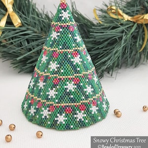 Puede incluir: Un árbol de Navidad con cuentas con una base verde, detalles de copos de nieve blancos y detalles rojos y dorados. El árbol tiene forma de cono y se encuentra sobre una superficie blanca. El texto "Snowy Christmas Tree" y "Beaded Treasury 2021" son visibles.