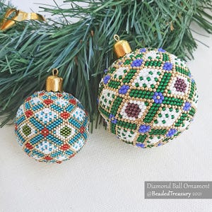 May include: Two beaded Christmas baubles with gold caps. One is teal, red, and white, the other green, white, and purple. The baubles have a diamond pattern and are near a sprig of evergreen. Text reads "Diamond Ball Ornament @BeadedTreasury 2021."