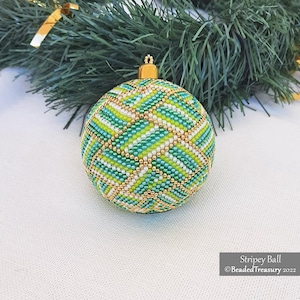 Puede incluir: Una bola de Navidad con cuentas con un diseño a rayas en tonos verdes, blancos y dorados. El adorno esférico tiene una tapa dorada. El fondo incluye una rama de pino verde y el texto "Stripey Ball" y "BeadedTreasury 2022".