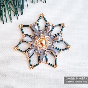 Op de afbeelding: Een met kralen versierde sneeuwvlok ornament met een stervorm. Het ornament heeft een gouden centrum, teal en gouden accenten en druppelvormige kralen. De tekst "Droplets Snowflake" en "BeadedTreasury 2023" zijn zichtbaar.