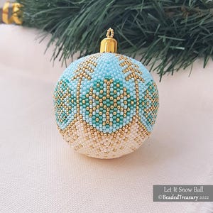 May include: A beaded Christmas bauble with a gold cap. The spherical ornament has a pattern of light blue, teal, gold, and white beads. The text "Let It Snow Ball" is visible on the bottom right.