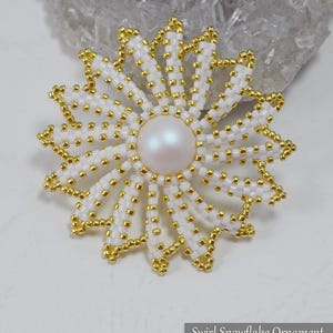 May include: A beaded snowflake ornament with a pearl center and white and gold beads. The ornament has a swirling design and is labeled "Swirl Snowflake Ornament @BeadedTreasury 2018".