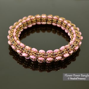 Può includere: Un braccialetto di perline rosa fatto a mano con dettagli dorati. Il braccialetto è composto da piccole perline rotonde e presenta un design a forma di fiore. Il braccialetto è mostrato su una superficie riflettente. Il testo "Flower Power Bangle" e "Beaded Treasury" è in basso a destra.