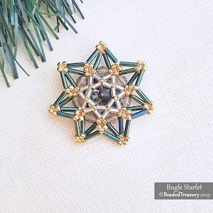 Op de afbeelding: Een handgemaakt stervormig kralenornament. Het ornament heeft een centraal ontwerp van grijze en zilveren kralen, omgeven door teal en gouden buiskralen. De tekst "Bugle Starlet" en "Beaded Treasury 2023" zijn zichtbaar.