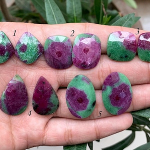 Könnte beinhalten: Sortiment aus zehn facettierten grünen und rosafarbenen Edelsteinen. Die Steine sind in verschiedenen Formen, darunter Birne, Oval und Quadrat. Die Steine sind von 1 bis 5 nummeriert.