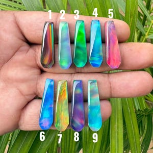 May include: Nine elongated, smooth, translucent cabochons with iridescent, swirling color patterns labeled one through nine. Each piece displays distinct hues including deep red, bright green, cyan, blue, yellow, and purple tones.