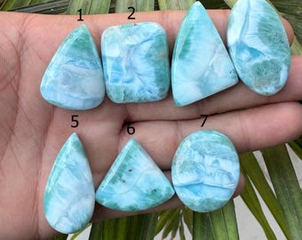 Peut inclure: Sept pierres précieuses de larimar polies de différentes formes, dont des gouttes, des rectangles, des triangles et des ovales. Les pierres présentent une gamme de motifs bleus et blancs, ressemblant à des vagues océaniques. Les pierres sont présentées sur un fond naturel.