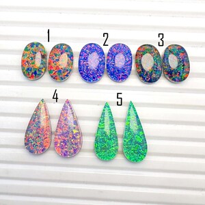 May include: A collection of ten cabochons arranged in five numbered pairs. The top row features six oval cabochons with multicolored, blue, and dark iridescent patterns. The bottom row displays four teardrop-shaped cabochons in pink, purple, and green.
