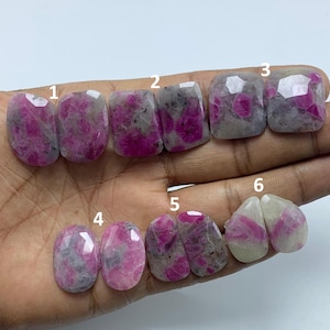 Peut inclure: Collection de six pierres précieuses rubis facettées de différentes formes. Les pierres présentent un mélange de teintes roses et grises, avec des inclusions visibles. Les pierres sont numérotées pour l'identification, mettant en valeur leurs motifs et tailles uniques.