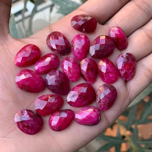 May include: A collection of 20 faceted ruby gemstones in a teardrop shape. The gemstones are a deep red color and have a high polish.