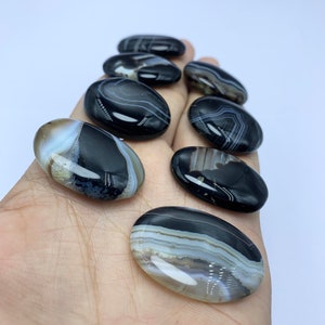 May include: A collection of eight black and white agate palm stones. The stones are smooth and polished, with a variety of patterns and swirls.