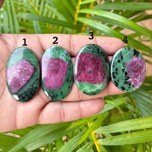 Puede incluir: Cuatro piedras de zoisita pulidas de forma ovalada con inclusiones de rubí, etiquetadas con los números 1, 2, 3 y 4. Cada piedra presenta un centro magenta rosado vibrante rodeado de patrones minerales moteados en verde y negro.
