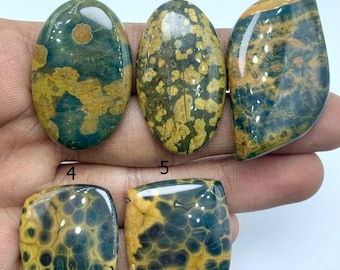 May include: Five polished gemstones in various shapes. The stones display a mix of colours, including deep teal, mustard yellow, and brown. The shapes include oval, teardrop, and square. The stones have a glossy finish and a unique, natural pattern.