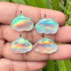 Pode incluir: Quatro cabochões translúcidos em forma de nuvem com um brilho iridescente semelhante ao arco-íris. Cada peça está etiquetada com um número preto de um a quatro. As superfícies exibem faixas de luz variáveis, refletindo tons de azul, verde, amarelo e laranja.