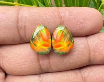 May include: Two teardrop-shaped cabochons featuring a vibrant play-of-colour with swirling patterns of bright orange, yellow, and green hues. These polished gemstones have a smooth, rounded surface and exhibit a distinct iridescent sheen across their entire face, reflecting light with a fiery, multi-coloured appearance.