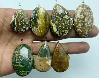 May include: Seven polished gemstones in various shapes and colours are displayed. The stones feature patterns of brown, green, yellow, and white. The shapes include teardrops and ovals, showcasing natural stone variations.