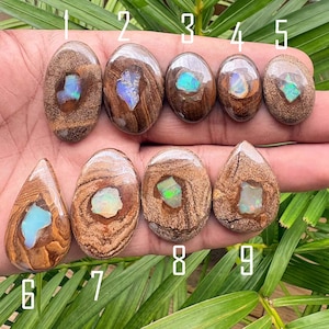 May include: Nine polished boulder opal cabochons arranged in two rows, each featuring a brown ironstone matrix with a central iridescent opal inlay. The stones vary in shape, including oval and teardrop forms, displaying flashes of blue and green.