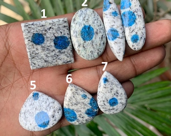 May include: A collection of seven K2 stone cabochons in various shapes. The stones feature a white and gray granite base with striking blue azurite inclusions. Shapes include rectangular, oval, and teardrop, showcasing the natural patterns.