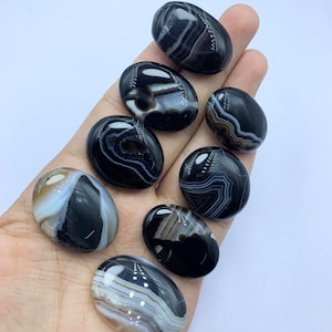 May include: Eight black and white agate oval cabochons with white banding. The cabochons are smooth and polished.