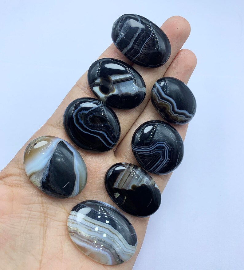 May include: Eight black and white agate oval cabochons with white banding. The cabochons are smooth and polished.