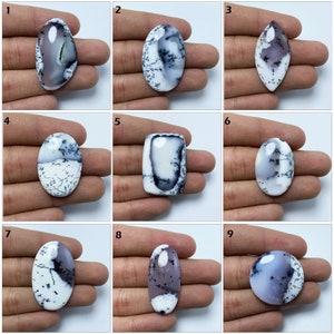 Peut inclure: Neuf cabochons ovales en opale dendritique avec des motifs blancs, gris et noirs. Les cabochons sont disposés en grille sur un fond blanc.