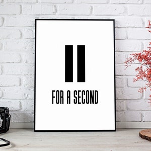 以下が含まれることがあります： 2本の黒い縦棒の下に「FOR A SECOND」というテキストが入った、黒と白の額入りプリント。左側にはヴィンテージカメラがあり、右側には赤い花の入った花瓶があります。背景は白いレンガの壁です。