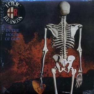 May include: A black and white album cover with a skeleton standing in the center. The album cover has the text "Toxic Reasons" in a circle with a cross and the letter "R" in the center. The text "In the House of God" is below the circle.