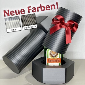 Könnte beinhalten: Ein dunkelgrauer Flaschenhalter im Industriestil in Form einer großen Mutter und Schraube, der eine Flasche Jägermeister hält. Der Bolzen ist mit einer roten Schleife verziert. Das Bild enthält den Text "Neue Farben!" und Farbmuster mit der Aufschrift "Silber" und "Dunkelgrau".