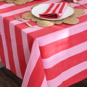 May include: A red and pink striped tablecloth with a matching napkin on a white plate. The table is set with a fork and several woven placemats. The overall theme is a bright and cheerful dining setting.