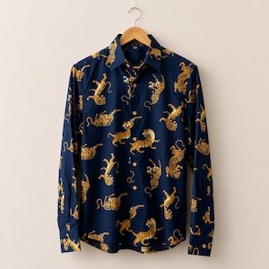 May include: Navy blue button-down shirt with a repeating pattern of gold tigers. The long-sleeved shirt is hanging on a wooden hanger. The shirt has a classic collar and buttoned cuffs.