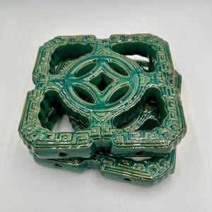 May include: A stack of three teal ceramic decorative blocks. Each block features a central circular design with a four-leaf clover pattern, surrounded by an intricate geometric border. The blocks have a glossy finish and are stacked on top of each other.