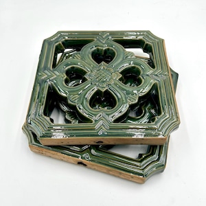 Puede incluir: Dos azulejos de cerámica verde con un diseño floral decorativo e intrincado. Los azulejos están apilados uno encima del otro.