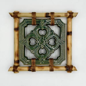 May include: A green ceramic tile with a decorative design is framed by four pieces of bamboo, tied together with twine.