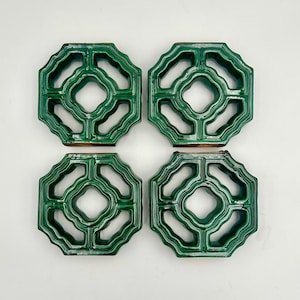 Puede incluir: Cuatro baldosas de cerámica verdes con un diseño calado. Cada baldosa tiene forma octogonal con un diamante central y cortes curvos. Las baldosas están dispuestas en un patrón cuadrado, mostrando su potencial decorativo.