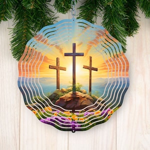 以下が含まれることがあります： 丘の上に3つの十字架が立つ夕焼けのシーンが描かれた金属製の風車。風車は円形の形をした層状のデザインで、下部に花柄が施されています。