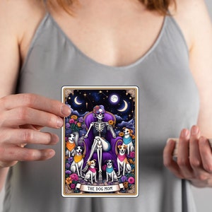 K&ouml;nnte beinhalten: Eine Tarotkarte mit einer farbenfrohen Illustration einer Skelettfrau mit lila Haaren, die auf einem Thron sitzt und von f&uuml;nf Hunden umgeben ist. Die Karte tr&auml;gt den Titel "The Dog Mom".