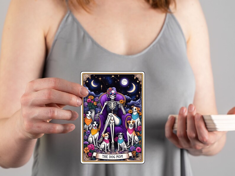 K&ouml;nnte beinhalten: Eine Tarotkarte mit einer farbenfrohen Illustration einer Skelettfrau mit lila Haaren, die auf einem Thron sitzt und von f&uuml;nf Hunden umgeben ist. Die Karte tr&auml;gt den Titel "The Dog Mom".