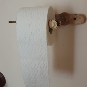 May include: A wooden toilet paper holder with a deer antler for the roll. The holder is mounted on a white wall.