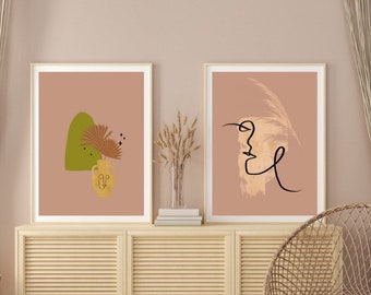 Op de afbeelding: Twee rechthoekige ingelijste kunstwerken met een oudroze achtergrond. De linker print toont een groene abstracte vorm, een gele vaas met een lijntekening van een gezicht en gedroogde palmbladeren. De rechter print toont een zwart lijnprofiel.