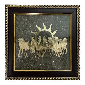 May include: A framed artwork featuring a gold-colored sun and seven horses. The horses are arranged in a line, appearing to be in motion. The background is a speckled, dark gray surface. The frame is dark brown with gold trim.