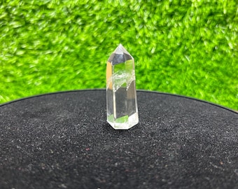 May include: A clear, six-sided quartz crystal point with a pointed top and a flat base. The crystal is transparent with visible internal fractures and inclusions, showcasing a natural geometric structure and a smooth, polished surface finish.