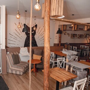 May include: A cat-themed cafe interior with wooden furniture, a rope hanging from the ceiling, and a cat scratching post. The cafe has a sign that says "KOCIE ZABAWY" which translates to "Cat Fun".