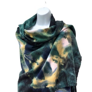 Op de afbeelding: Een sjaal met een abstract print in groen, blauw, geel en roze. De sjaal is gevouwen en gedrapeerd over een mannequin.