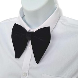 Può includere: Un papillon in velluto nero dalla forma distintiva, posto su una camicia bianca. Il papillon è centrato e sembra essere realizzato in un materiale morbido e lussuoso, perfetto per occasioni formali.