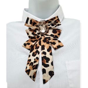 May include: A brown and white leopard print bow tie with a large clear rhinestone brooch.