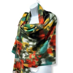 May include: A colorful scarf with a green, yellow, orange, and black abstract pattern. The scarf has fringe on the ends.