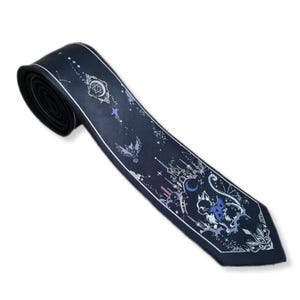 May include: Navy blue necktie with a celestial design. The tie features white and light blue illustrations of stars, a crescent moon, a castle, and a cat with wings. The tie is made of a smooth fabric and has a pointed end.